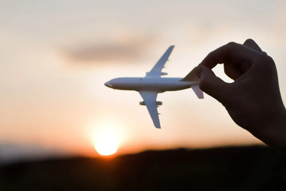 Person holding toy plane up against a sunset sky